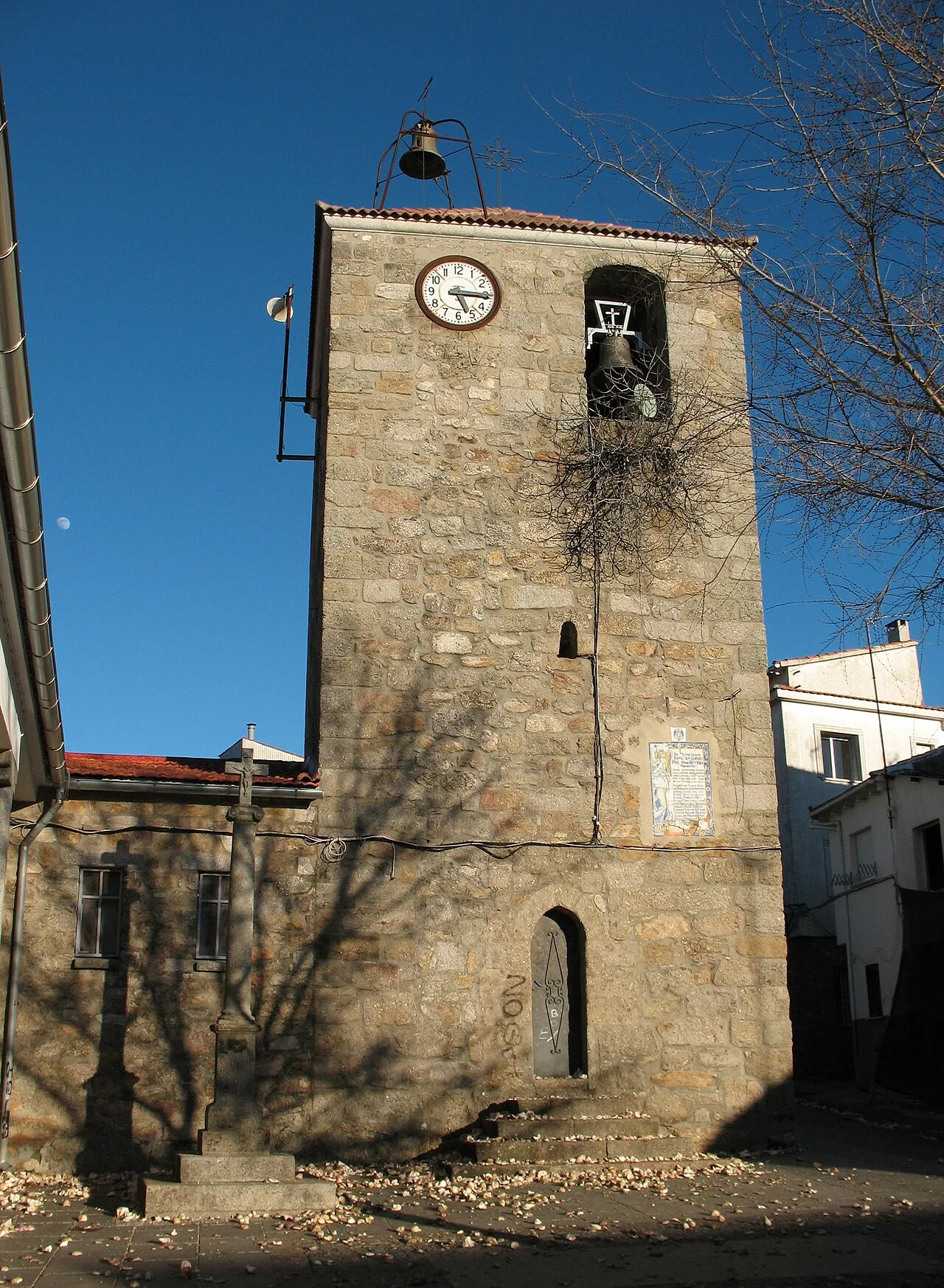 Torre de iglesia de piedra con reloj y campanario en Piornal.