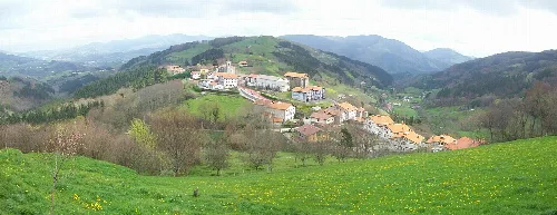 Blick auf Alkiza mit Häusern in einem Tal, umgeben von grünen Bergen.