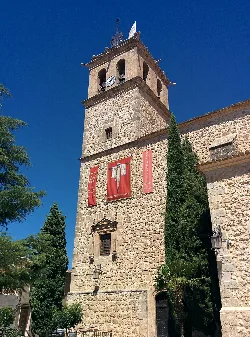 Torre de piedra de una iglesia con reloj y bandera en La Puebla de Almoradiel.
