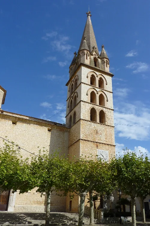 Kirchturm mit Bögen und einer Uhr an der Basis, unter einem blauen Himmel.