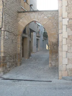 Steinbogen in Juneda, der zu einer steilen, schmalen Straße führt.