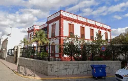 Building with white and red walls, surrounded by plants and a wrought iron fence in Santa Marta de los Barros.