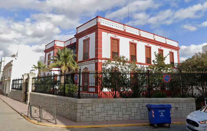 Gebäude mit weißen und roten Wänden, umgeben von Pflanzen und einem schmiedeeisernen Zaun in Santa Marta de los Barros.