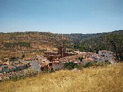 Vista de un pueblo con tejados y colinas verdes en el fondo.