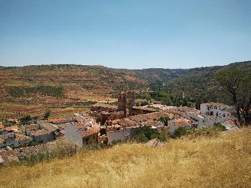 Vista de un pueblo con tejados y colinas verdes en el fondo.