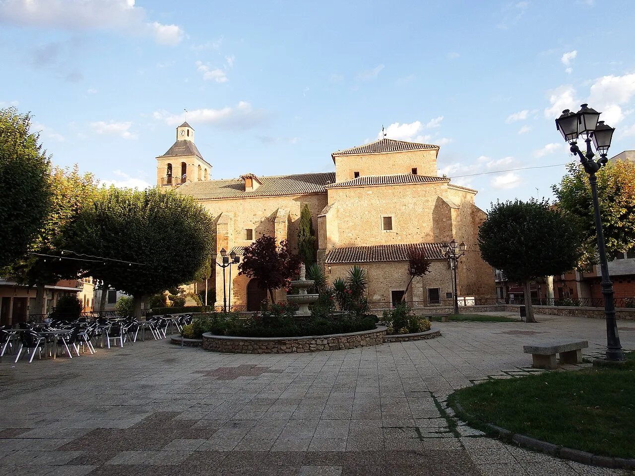 Church in Pozuelo de Calatrava with trees and benches in the square.