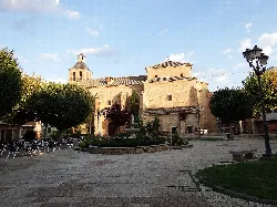 Church in Pozuelo de Calatrava with trees and benches in the square.