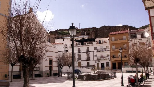 Platz mit Bäumen, Laternen und weißen sowie beigen Gebäuden in Zújar, Granada.