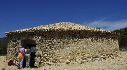 Round stone building with a tiled roof and people looking inside.