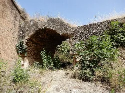 Restos de un arco de piedra en un entorno natural con vegetación.