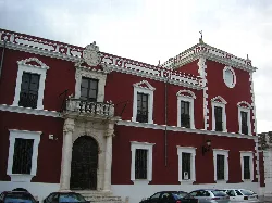 Edificio con fachada roja, ventanas con marcos blancos y entrada con arco en Fernán Núñez.