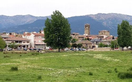 Vista de un pueblo con árboles, montañas y un campo verde.