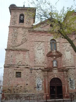 Fachada de una iglesia con campanario y detalles en piedra y ladrillo en Herencia.
