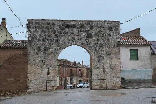 Stone city gate in Villahoz with houses around.