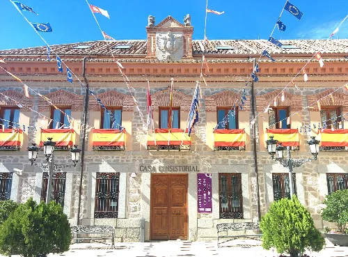 Facade of Sonseca town hall with flags and wooden door.
