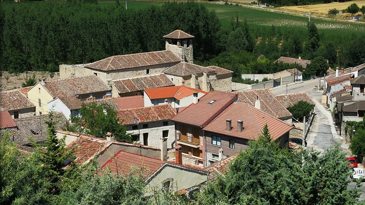 Houses and a historic building in Fuentidueña, Segovia, surrounded by greenery.