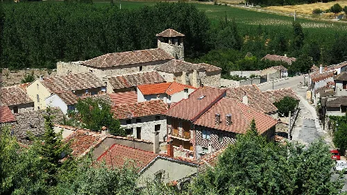 Houses and a historic building in Fuentidueña, Segovia, surrounded by greenery.