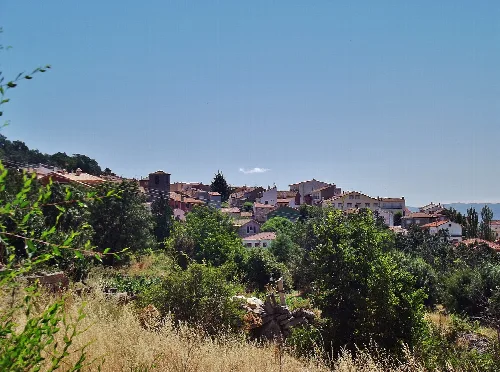 Landschaft von Hoyocasero mit Häusern und Bäumen unter einem blauen Himmel.