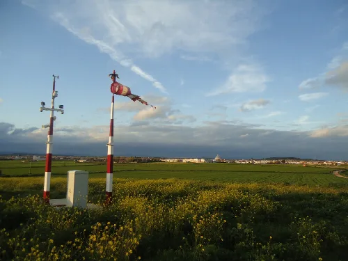 Vista del helipuerto y el pueblo en la distancia con cielo azul y nubes.