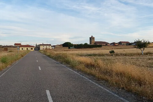 Ländliche Straße mit Blick auf das Dorf und eine Kirche im Hintergrund.