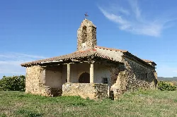 Iglesia de piedra con torre y porche en un campo verde.