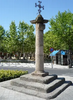 Stone pillory in the square with trees and market stalls.