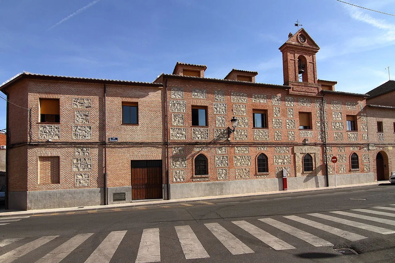 Edificio de ladrillo con ventanas y una pequeña torre en la esquina, en Fuensalida.