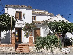 Edificio de una antigua escuela con paredes blancas y plantas en el jardín.