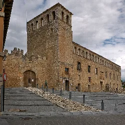 Fachada de un antiguo palacio de piedra con torre y ventanas pequeñas.