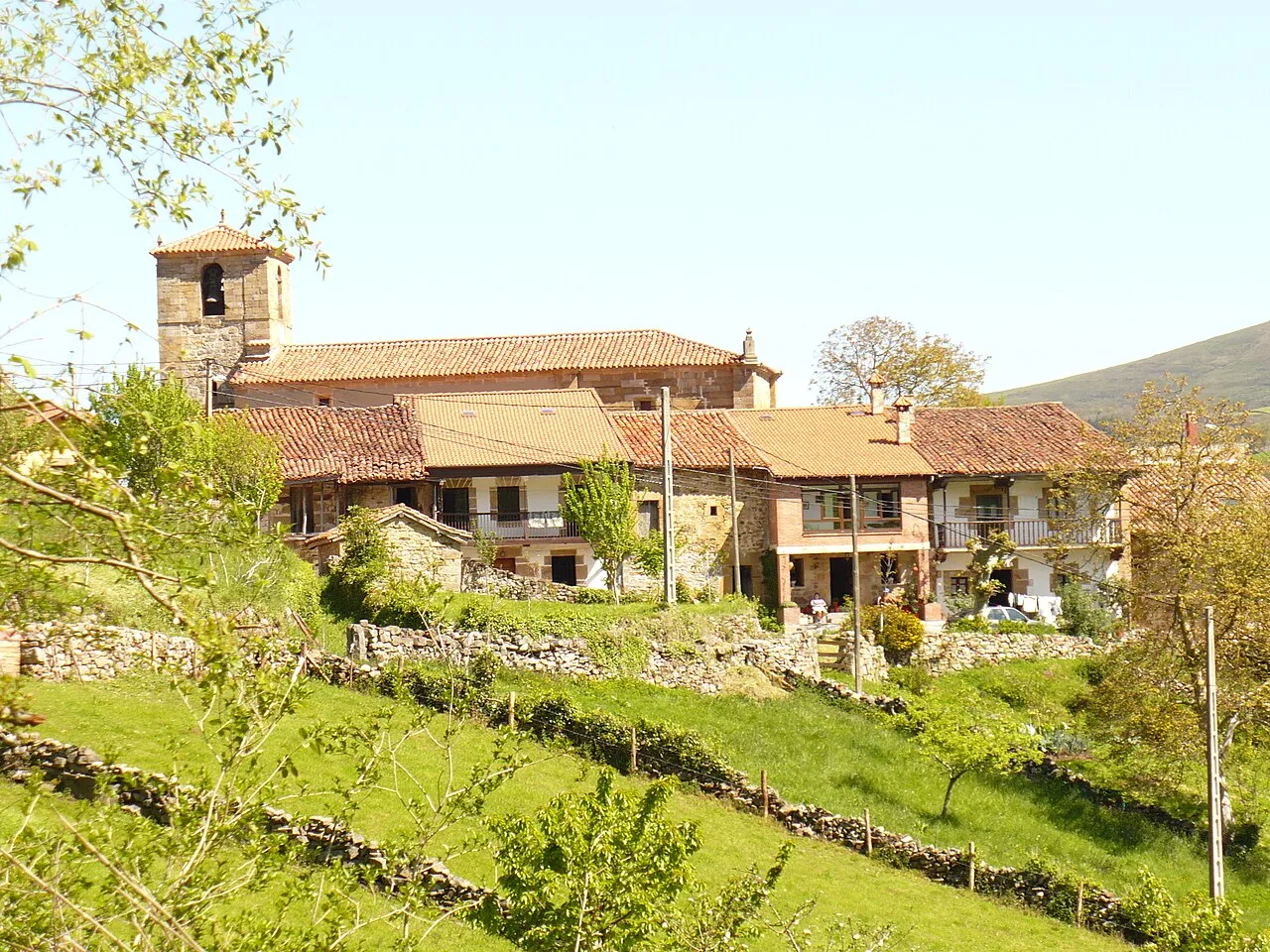 Casas y una iglesia en un pueblo rodeado de vegetación y colinas.