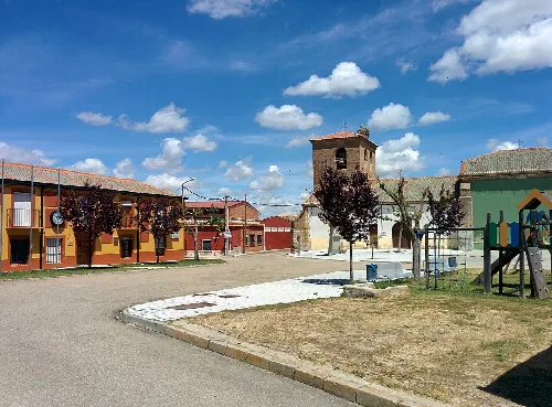 Iglesia de San Miguel Arcángel en Ramiro, Valladolid, con casas y un campanario bajo un cielo azul.