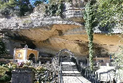 Sanctuary in Piloña with entrance and stairs in front of a large rocky overhang.