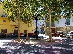 Square with trees, cars, and a fountain in the center in Soneja.