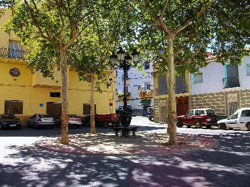 Plaza con árboles, coches y una fuente en el centro en Soneja.