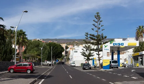 Straße in Fasnia mit Bäumen, Autos und Tankstelle.