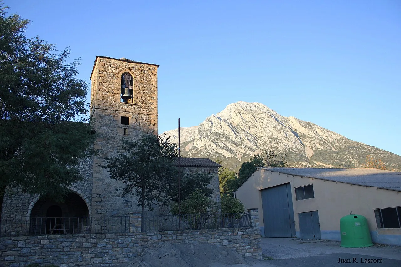 Romanische Kirche mit Turm und Bergen im Hintergrund.