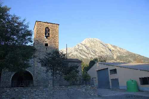 Romanische Kirche mit Turm und Bergen im Hintergrund.
