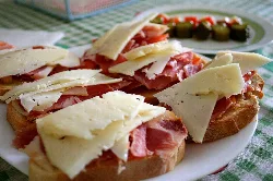 Tostas con jamón y queso en Hellín con aceitunas al fondo.