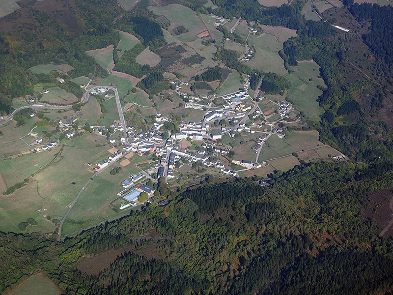 Luftaufnahme eines Ortes mit Gebäuden und Straßen in einem von Bäumen umgebenen Tal.