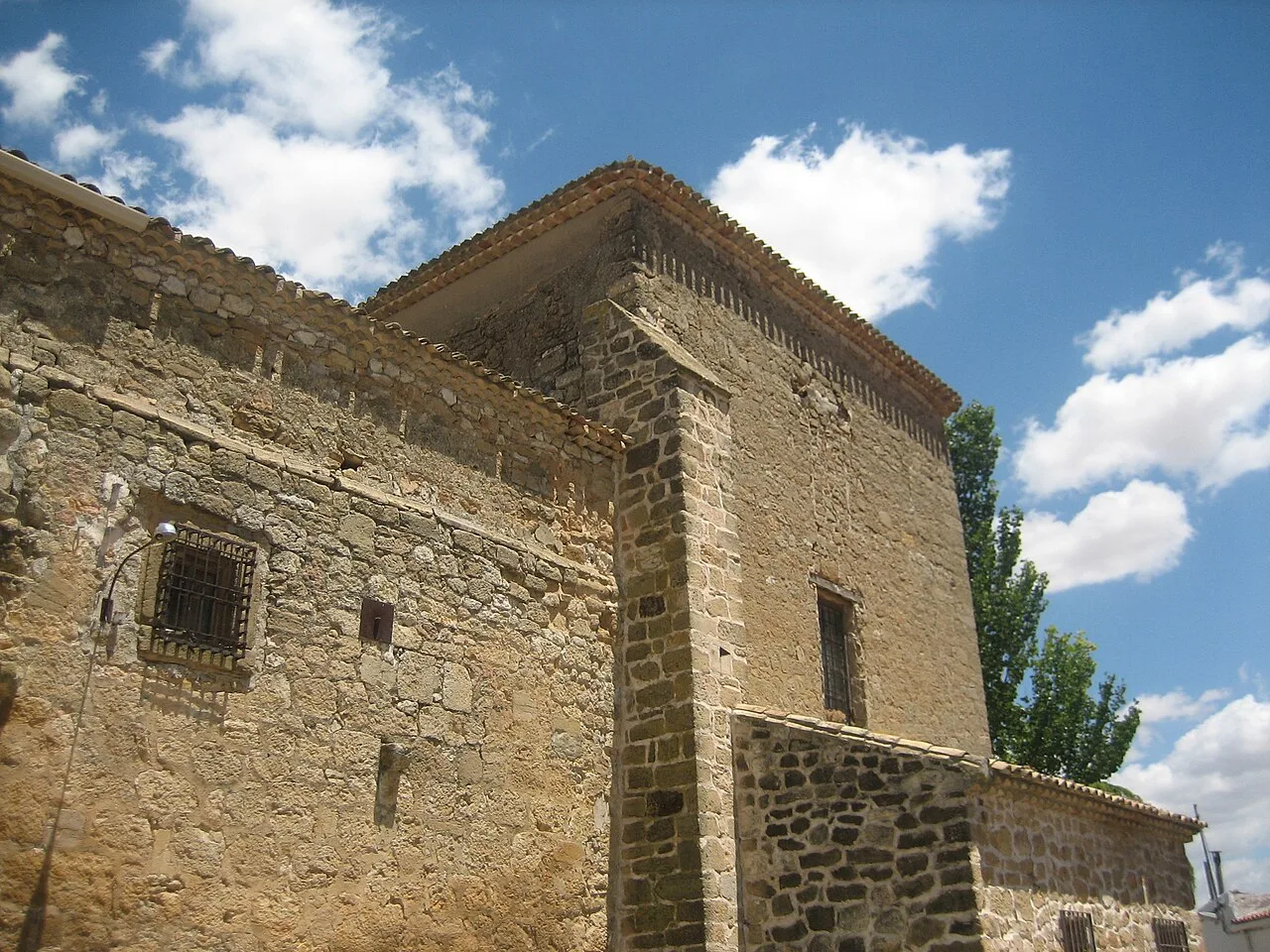 Cabecera de una iglesia de piedra con ventanas pequeñas y cielo azul con nubes.