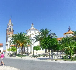 Iglesia blanca con cúpula y torre en Valsequillo, Córdoba, con palmeras y árboles alrededor.