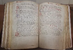 Manuscrito antiguo en pergamino con tinta negra y roja, abierto en un libro.