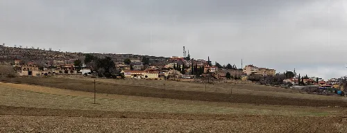 Rural landscape with fields and town on the horizon under cloudy sky.