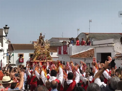 People in a procession with a religious figure on a decorated float with flowers.