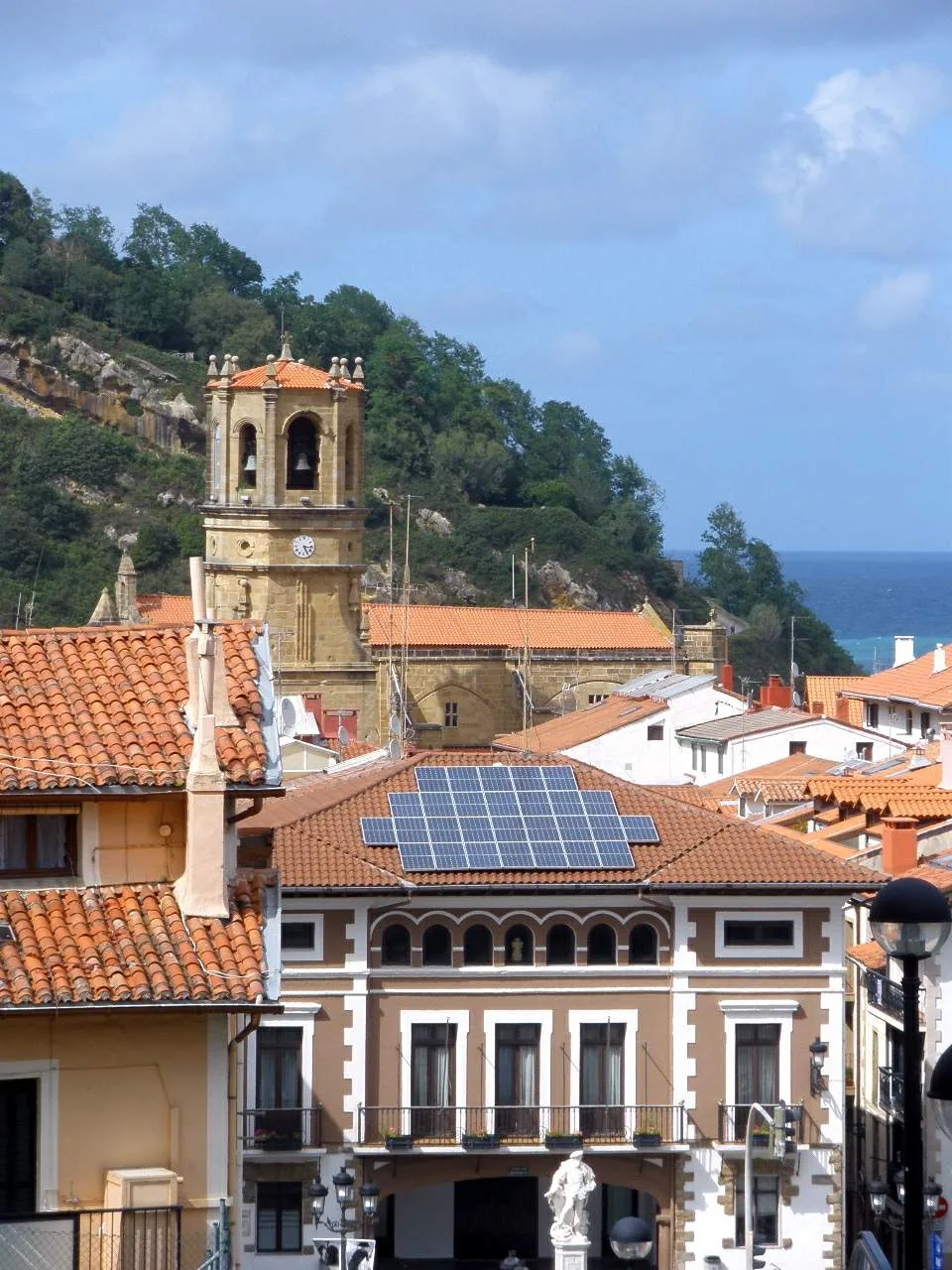 Casas con tejados de tejas y paneles solares, iglesia y mar en el fondo en Guetaria.
