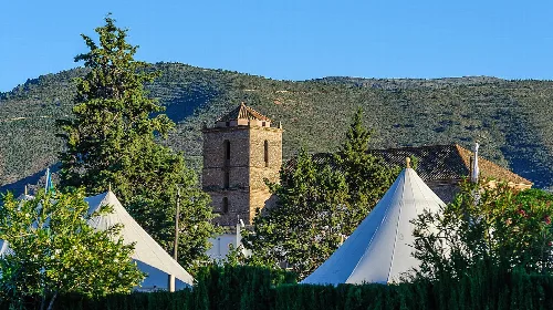 Iglesia de Santa María la Mayor en Padules, rodeada de tiendas de campaña y árboles.