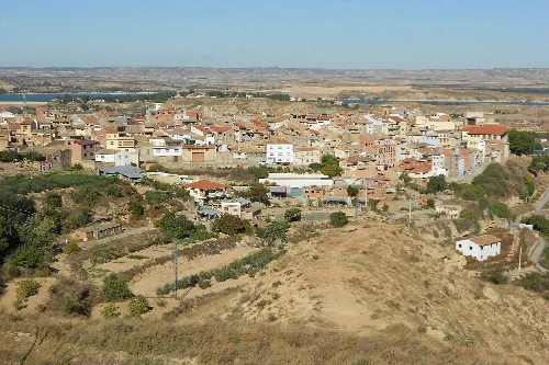 Panoramic view of Caspe with houses, hills, and river in the background.