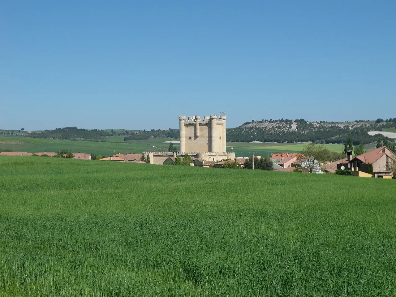 Castillo en Fuensaldaña con campos verdes y cielo azul.