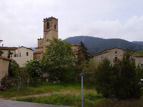 Blick auf die Kirche Sant Muç in Cànoves, mit Häusern und Bäumen drumherum.