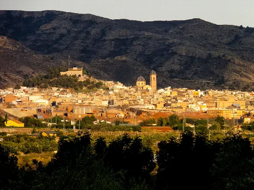 Blick auf Agost, Alicante, mit Kirchen und Häusern im Tal, umgeben von Bergen.